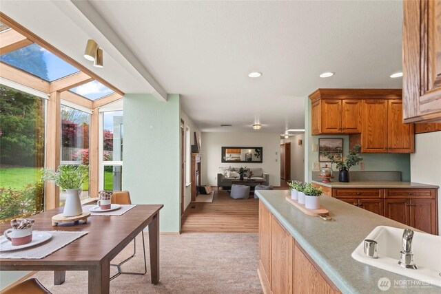 kitchen featuring brown cabinets, a sink, light countertops, light carpet, and recessed lighting