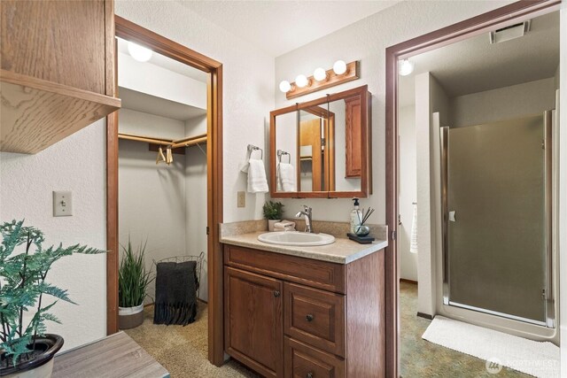 full bath featuring visible vents, vanity, a textured wall, a walk in closet, and a shower stall