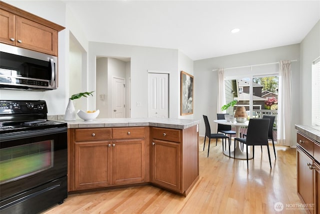 kitchen with stainless steel microwave, brown cabinets, light wood-type flooring, black electric range, and a peninsula