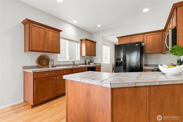 kitchen featuring light wood-style flooring, brown cabinetry, black appliances, a sink, and a peninsula