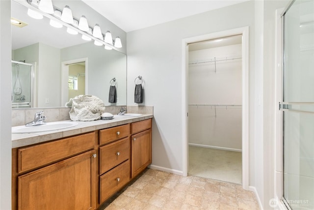 full bath featuring a stall shower, double vanity, a sink, and a spacious closet