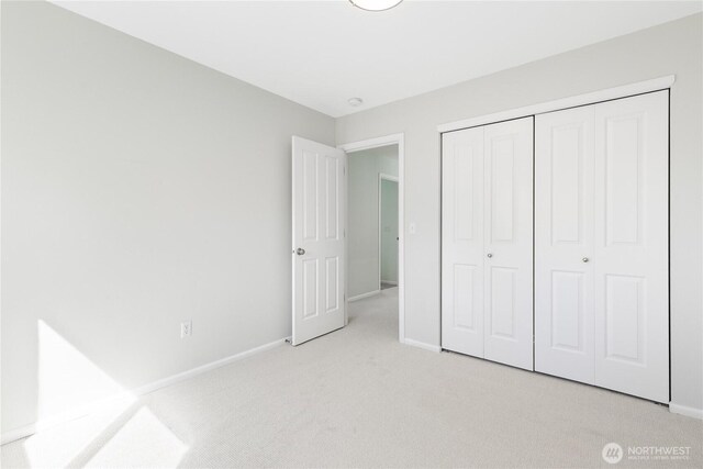 unfurnished bedroom featuring a closet, light colored carpet, and baseboards