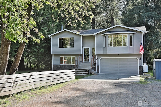split foyer home with concrete driveway, a garage, and stone siding