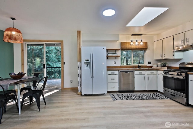 kitchen featuring stainless steel appliances, a skylight, light wood-type flooring, decorative light fixtures, and under cabinet range hood