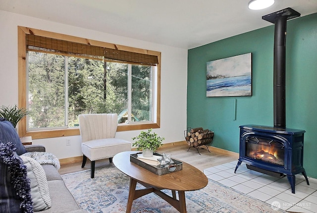 living area featuring baseboards, a wood stove, a healthy amount of sunlight, and light wood-style floors