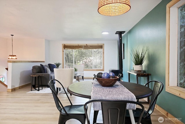 dining space with a wood stove, light wood-type flooring, and baseboards