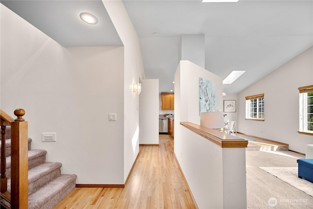 corridor featuring vaulted ceiling with skylight, an upstairs landing, light wood finished floors, baseboards, and visible vents