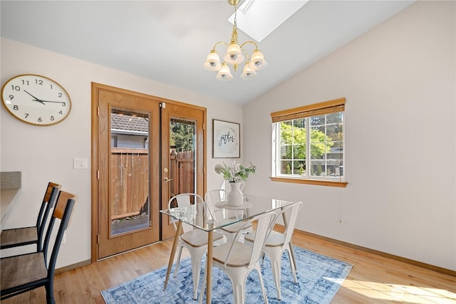 dining area with an inviting chandelier, vaulted ceiling with skylight, light wood-style flooring, and baseboards