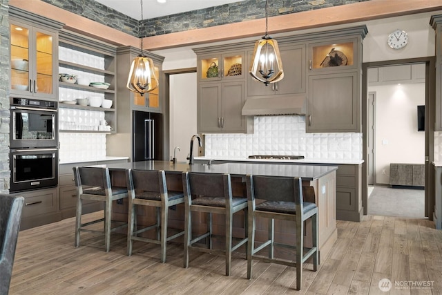 kitchen with double oven, tasteful backsplash, under cabinet range hood, a sink, and high end black fridge