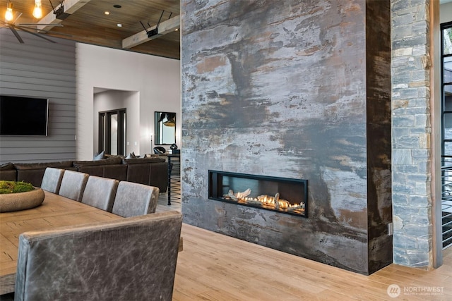 living room with a towering ceiling, a large fireplace, beam ceiling, wood ceiling, and wood finished floors