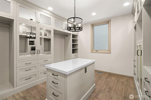 spacious closet with a chandelier, light wood-style flooring, and visible vents