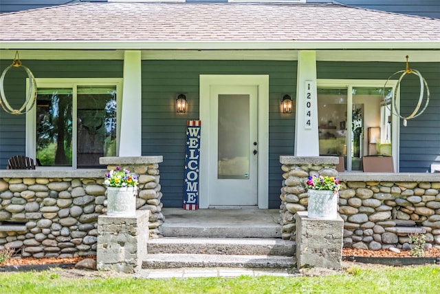 entrance to property with a shingled roof and covered porch