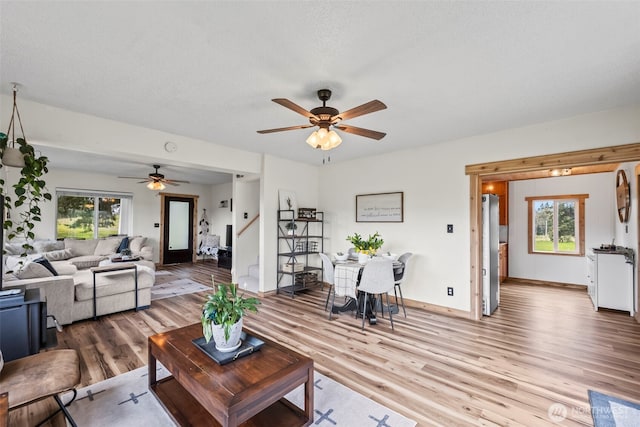 living area with a wealth of natural light, a ceiling fan, wood finished floors, and baseboards
