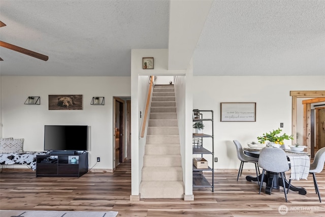 stairway with wood finished floors, a textured ceiling, and ceiling fan