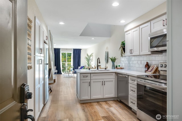 kitchen featuring a sink, light countertops, appliances with stainless steel finishes, light wood-style floors, and a peninsula