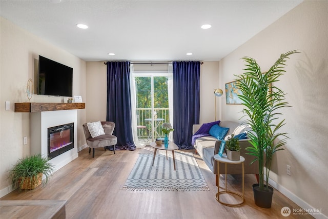 living area with a glass covered fireplace, baseboards, and wood finished floors
