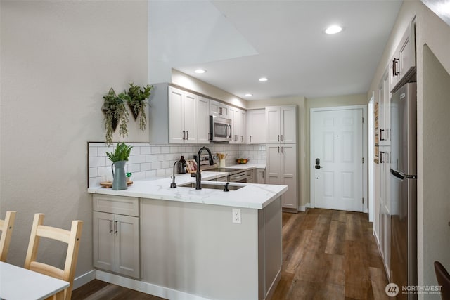 kitchen featuring a peninsula, recessed lighting, appliances with stainless steel finishes, dark wood-style flooring, and decorative backsplash