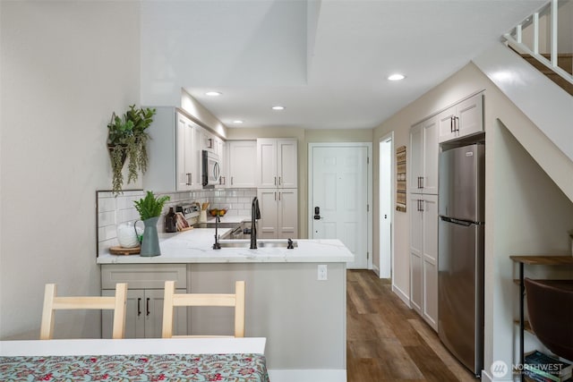 kitchen with appliances with stainless steel finishes, a peninsula, backsplash, dark wood finished floors, and a sink