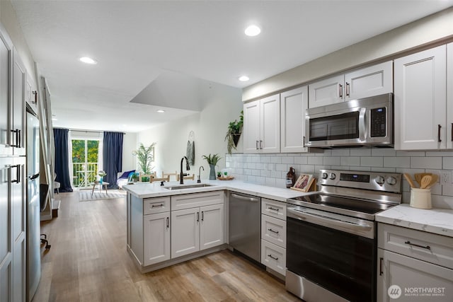 kitchen with stainless steel appliances, a peninsula, a sink, and backsplash