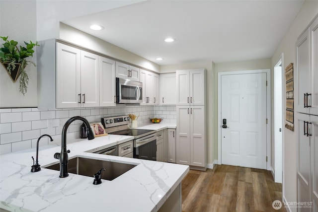 kitchen featuring light stone counters, wood finished floors, a sink, stainless steel appliances, and backsplash