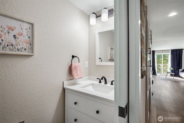 bathroom with wood finished floors, recessed lighting, vanity, and a textured wall