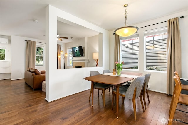 dining room featuring a wall mounted air conditioner, wood finished floors, a ceiling fan, baseboards, and a fireplace