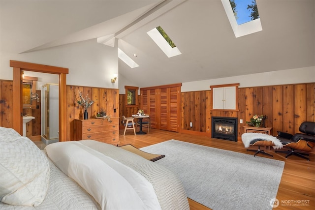 bedroom featuring a skylight, wooden walls, wood finished floors, a glass covered fireplace, and a wainscoted wall