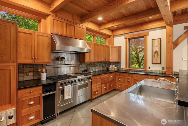 kitchen with stainless steel counters, under cabinet range hood, gas stove, wood ceiling with exposed beams, and a sink