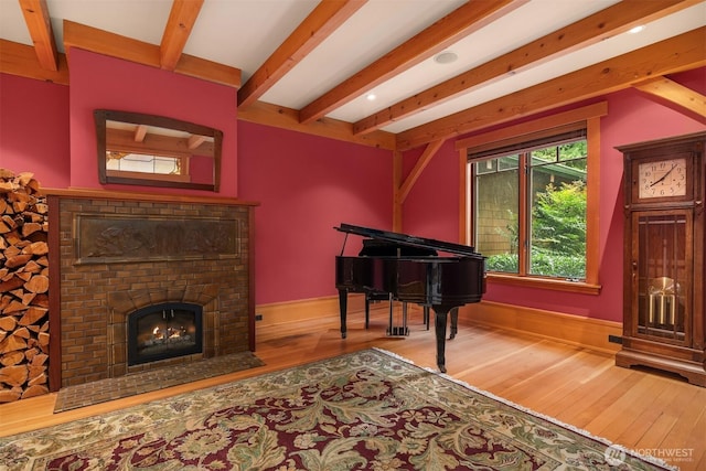 living area featuring beamed ceiling, wood finished floors, baseboards, and a brick fireplace