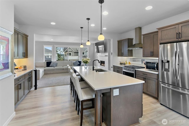 kitchen with light wood-style floors, open floor plan, recessed lighting, wall chimney exhaust hood, and stainless steel appliances