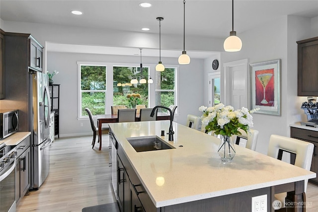 kitchen with a kitchen island with sink, appliances with stainless steel finishes, light wood-type flooring, a sink, and baseboards