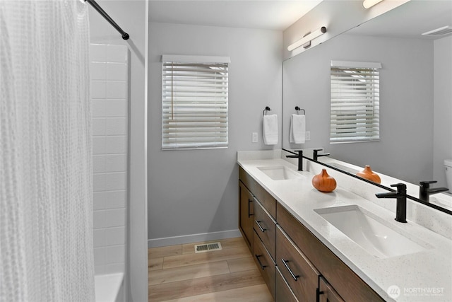 bathroom with a sink, baseboards, double vanity, and wood finished floors