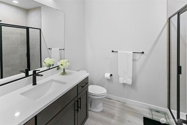 full bath featuring a stall shower, wood finished floors, vanity, baseboards, and toilet