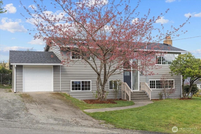 bi-level home featuring roof with shingles, an attached garage, driveway, and a front lawn