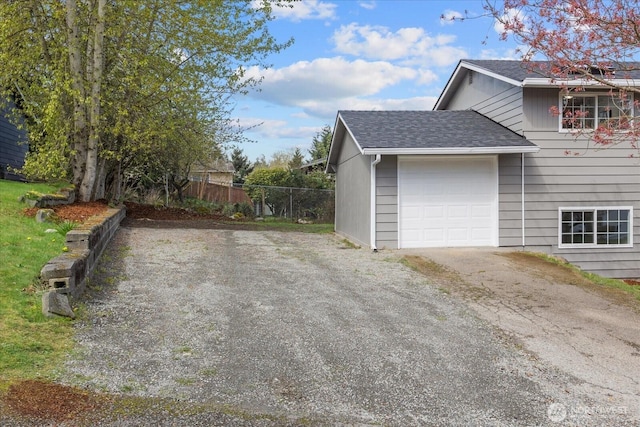 view of side of home featuring driveway, a garage, fence, and roof with shingles