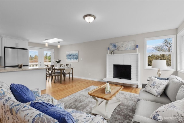 living room featuring a fireplace, light wood-style floors, baseboards, and a skylight