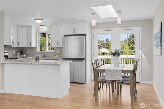 kitchen with white cabinets, appliances with stainless steel finishes, a peninsula, light wood finished floors, and a skylight