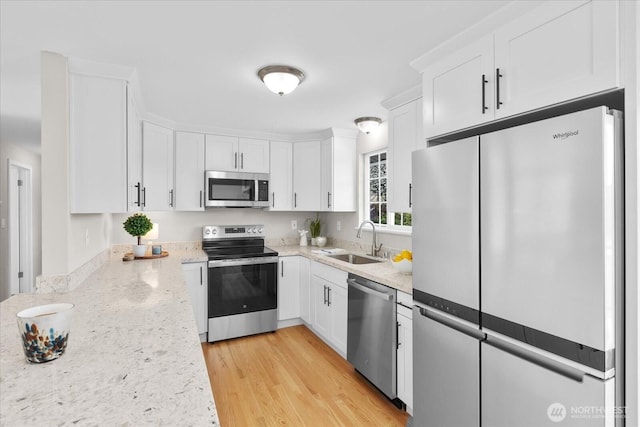 kitchen featuring white cabinets, a sink, appliances with stainless steel finishes, light wood finished floors, and light stone counters