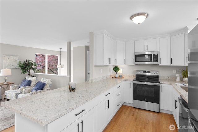 kitchen with a peninsula, white cabinetry, light stone countertops, light wood-style floors, and appliances with stainless steel finishes