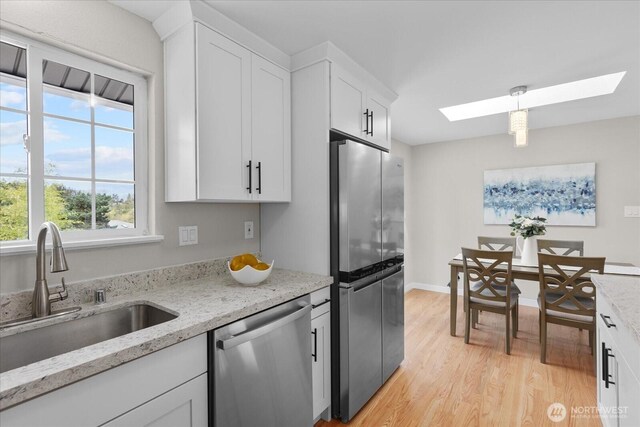 kitchen with light wood-type flooring, white cabinetry, a skylight, stainless steel appliances, and a sink