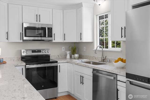 kitchen with appliances with stainless steel finishes, a sink, white cabinetry, and light stone countertops