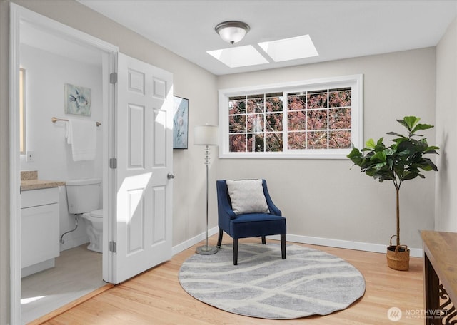 living area featuring light wood-style flooring, a skylight, and baseboards