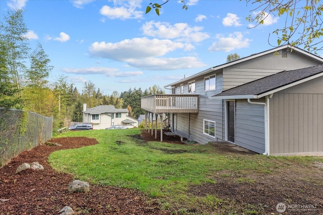 rear view of house featuring a deck, a shingled roof, fence, and a lawn