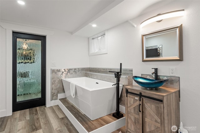 bathroom featuring vanity, a freestanding tub, wood finished floors, tile walls, and recessed lighting
