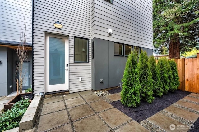 view of exterior entry with fence and a patio