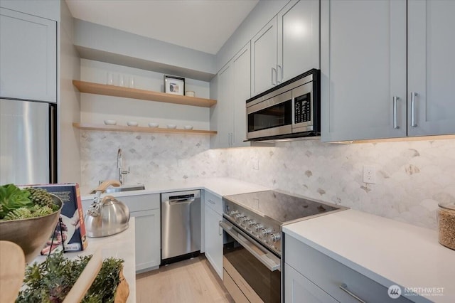 kitchen featuring appliances with stainless steel finishes, light wood-style flooring, light countertops, decorative backsplash, and a sink