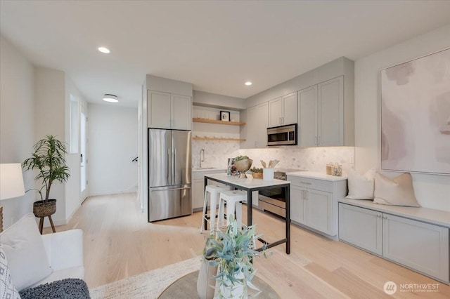 kitchen with tasteful backsplash, open shelves, a sink, stainless steel appliances, and light wood finished floors