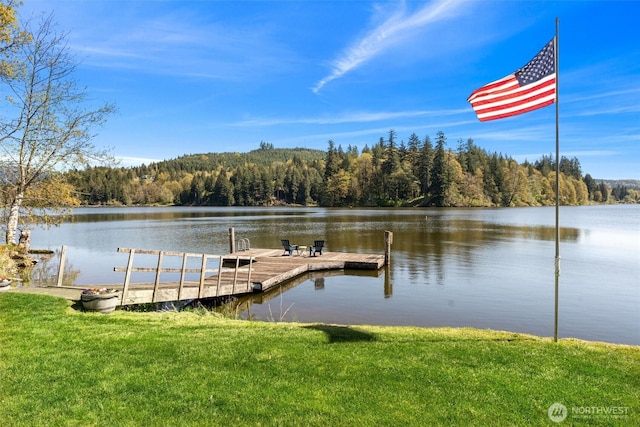 view of dock with a view of trees, a lawn, and a water view