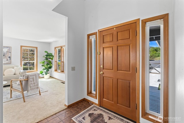 foyer entrance with dark colored carpet, baseboards, a wealth of natural light, and dark tile patterned flooring