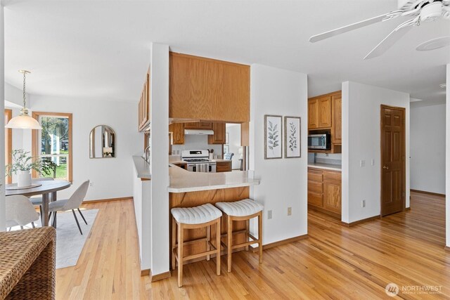 kitchen featuring stainless steel microwave, light wood-style floors, white range with gas cooktop, light countertops, and under cabinet range hood